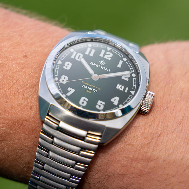 Silver wristwatch with a dark face on a wrist against a blurred green background