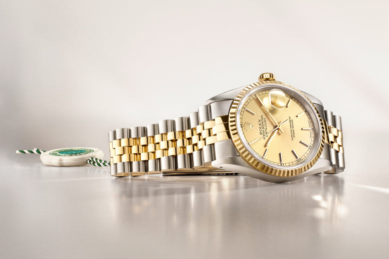 Rolex watch with gold and silver band on a light grey background