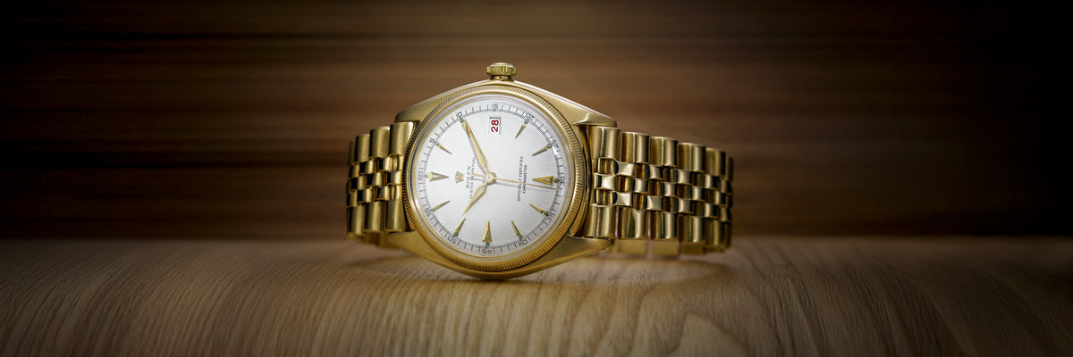 Rolex Gold wristwatch on a wooden surface with a dark brown background