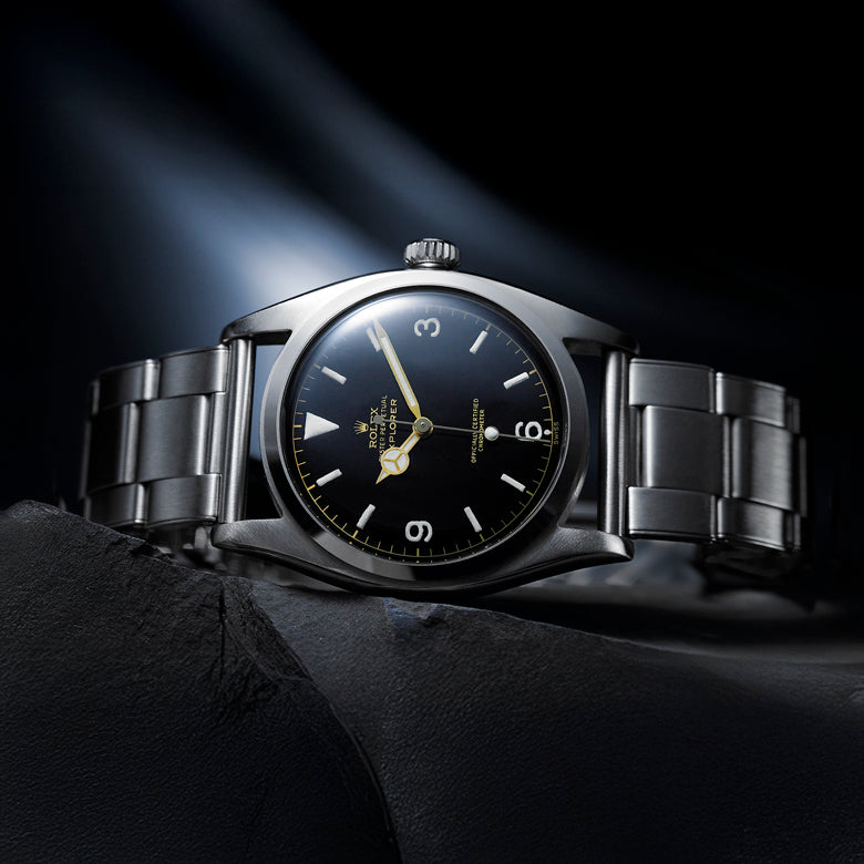 Rolex watch with black dial and silver metal strap on a dark background