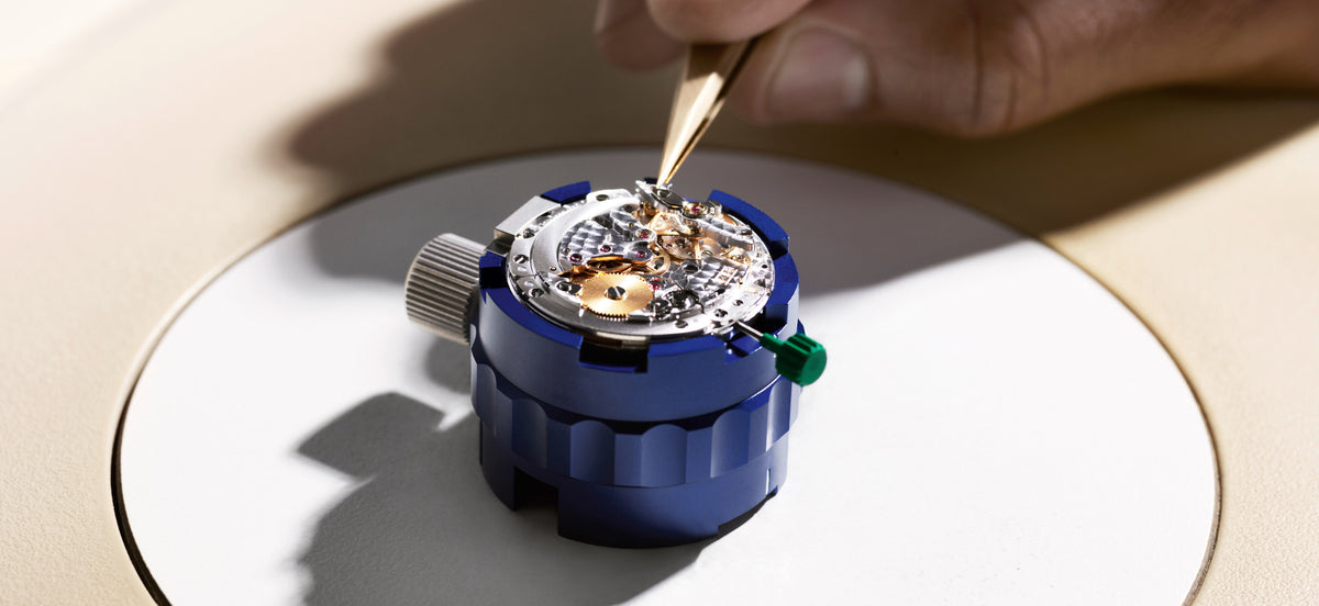 Person working on a watch mechanism with a tool on a white surface