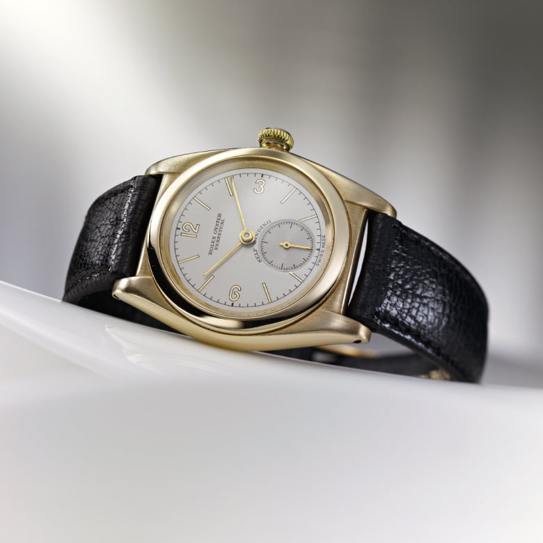 Rolex Gold wristwatch with black leather strap on a white surface