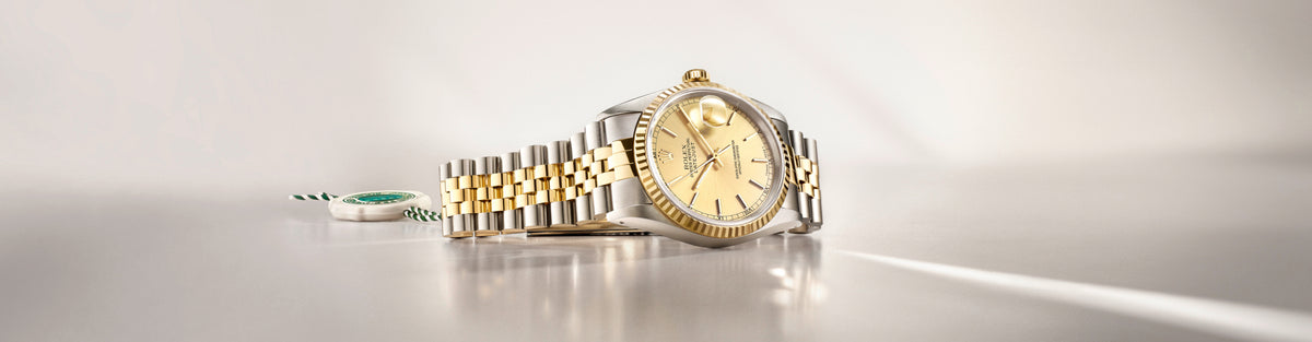 Rolex Gold and silver watch on a reflective surface with a light gray background