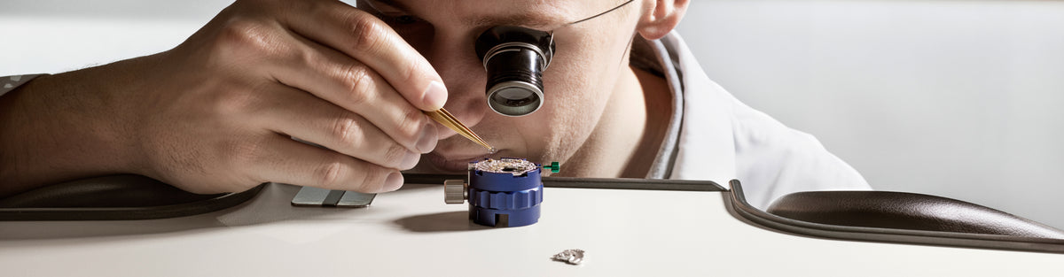 Person using a magnifying glass to examine a Rolex movement on a white surface
