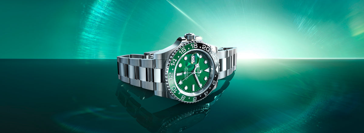 Silver Rolex watch with green face on a reflective surface.