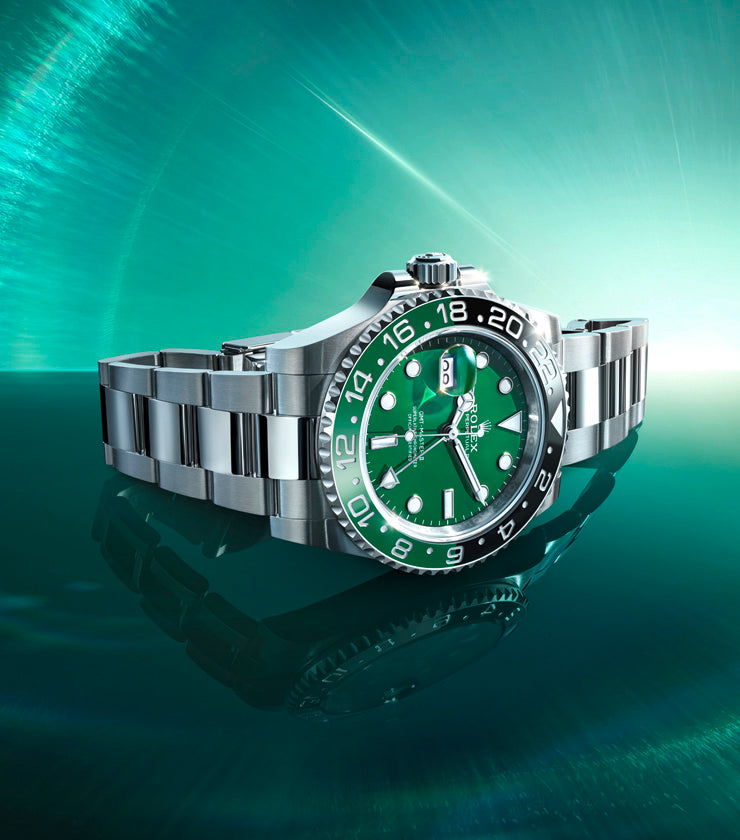 Silver Rolex watch with a green face on a reflective green surface.